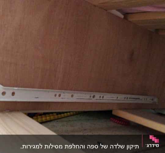 מסילת מתכת מחוברת ללוח עץ מתחת למיטה